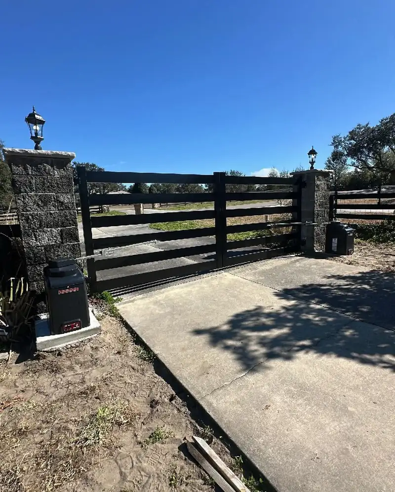 Stone columns with lanterns beside a black four-board driveway gate