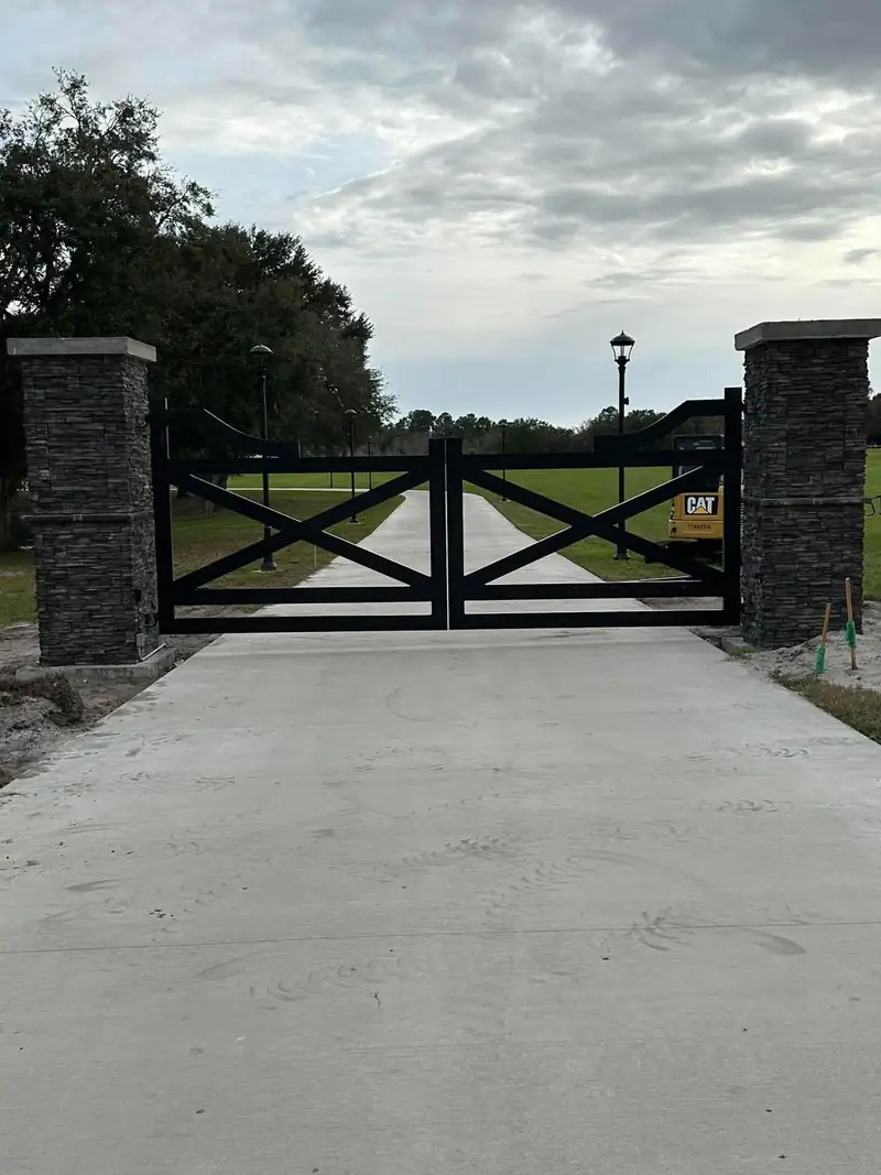 Stacked-stone columns framing a black X-pattern double gate on a concrete drive