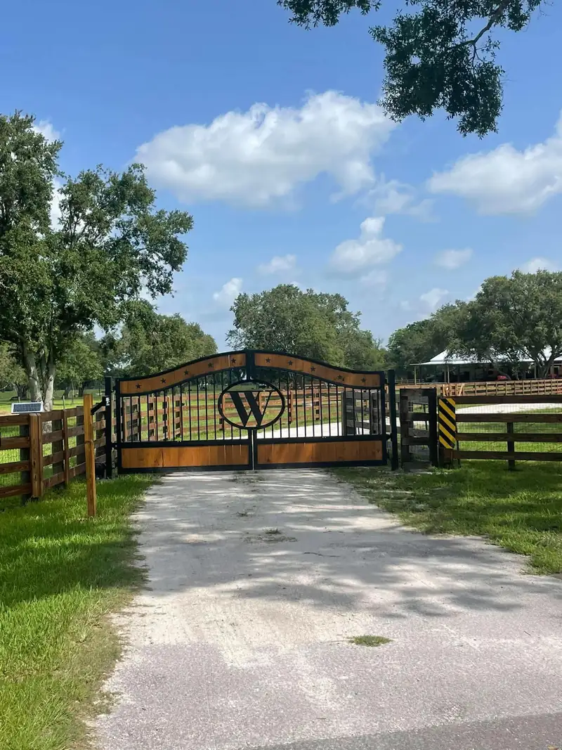 Double driveway gate with wood panels, star cut-outs and a W monogram at a ranch entrance